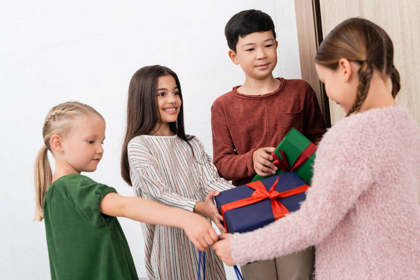Multiethnic kids giving presents to blurred friend at home  - Foto, afbeelding
