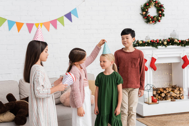 Mezirasové děti držící party čepice během narozeninové párty a Vánoce doma  - Fotografie, Obrázek