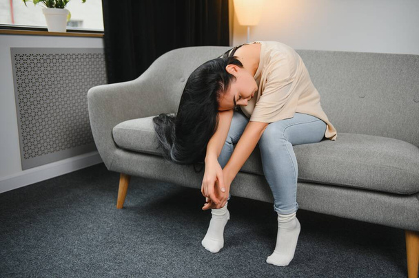 Depressed sad attractive woman crying on sofa couch at home feeling lonely tired and worried suffering depression in mental health, loneliness and isolation concept. Psychology, solitude and people - 写真・画像