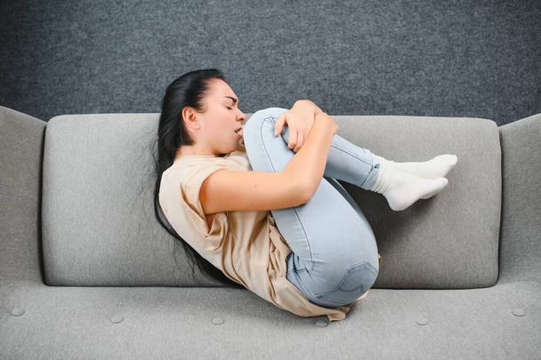 Beautiful hispanic woman in painful expression holding her belly suffering menstrual period pain lying sad on home bed having tummy cramp in female health concept. - Foto, immagini