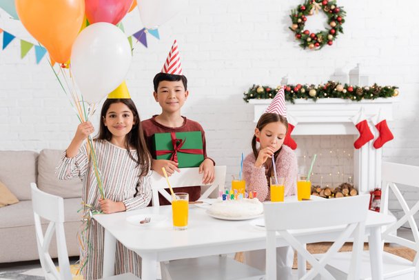 Мультиэтнические дети держат воздушные шары и подарят торт на день рождения дома зимой - Фото, изображение