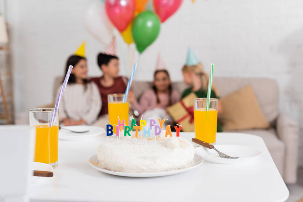 Birthday cake and orange juice on table near blurred kids at home  - Photo, Image