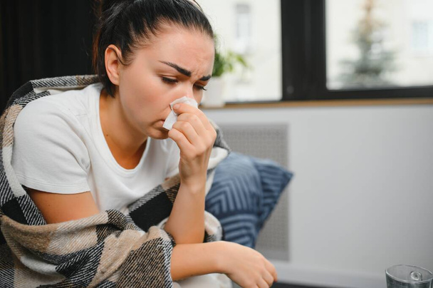 healthcare, cold, allergy and people concept - sick woman blowing her runny nose in paper tissue at home - Fotoğraf, Görsel