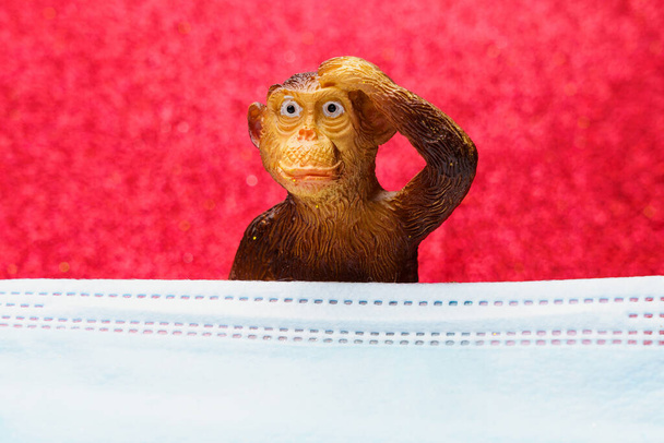 Figur eines Affen hinter einer medizinischen Chirurgenmaske. Das Konzept der Pocken oder Affenpocken. Hintergrund mit Kopierraum für Text - Foto, Bild