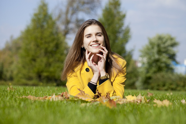 Happy young woman in yellow coat in autumn park - Fotó, kép