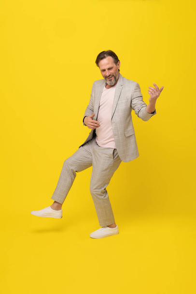 Middle aged business man musician pretend playing guitar happy smiling isolated on yellow background. Handsome mature businessman in white suit. Business concept. Music concept.  - Photo, image