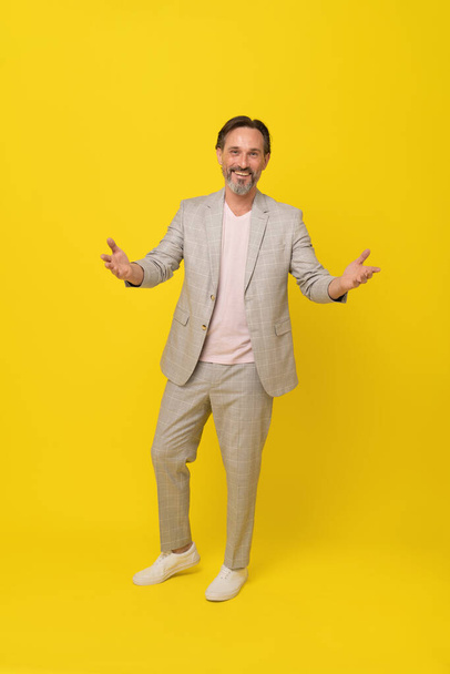 Business people, handsome middle aged businessman spread hands in white suit. Mature business man in white, grey casual suit looking at camera isolated on yellow background. Elegant business man.  - Фото, изображение