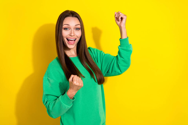 Photo portrait of stunning young girl raise fists celebrate success dressed trendy green sweatshirt isolated on yellow color background. - Photo, image