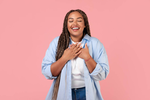 Grateful African American Woman Pressing Hands To Chest Standing Posing With Eyes Closed Over Pink Background. Studio Shot Of Obese Lady Expressing Gratitude. Happiness And Kindness Concept - Photo, Image