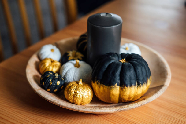 Black pumpkin halloween thanksgiving decor. Decorative modern minimal indoor composition with black, golden pumpkins in wooden plate at table. - Fotó, kép