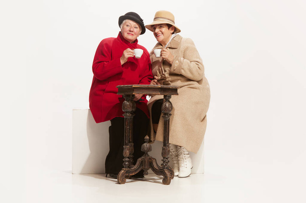 Twee elegante oudere vrouwen in retro stijl herfstkleding geïsoleerd op witte achtergrond. Concept van schoonheid, oude generatie, mode, emoties. Kopieer ruimte voor advertentie - Foto, afbeelding