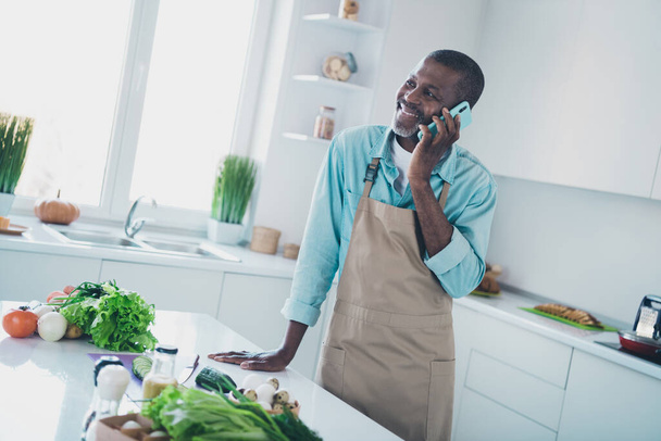 Photo of positive cheerful age man wear apron preparing supper talking modern device indoors room home. - Foto, afbeelding