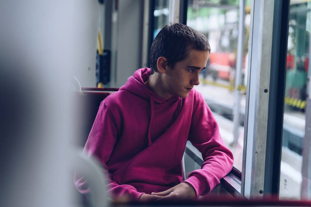 Teenage boy in a pink hooded sweatshirt, pensive, sad, is traveling by bus - 写真・画像