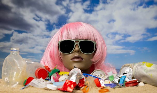Plastová samičí figurína hlava uvízla v písku s pláží plnou odpadků a odpadků - Fotografie, Obrázek