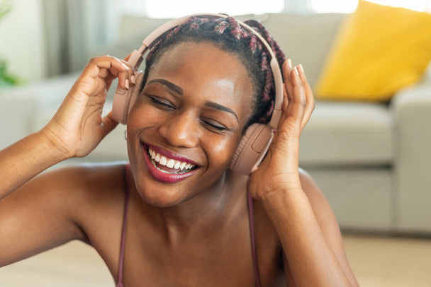 Enjoying favorite playlist during home workout. Happy black woman wearing wireless headphones and listening to music with closed eyes, closeup shot - Valokuva, kuva