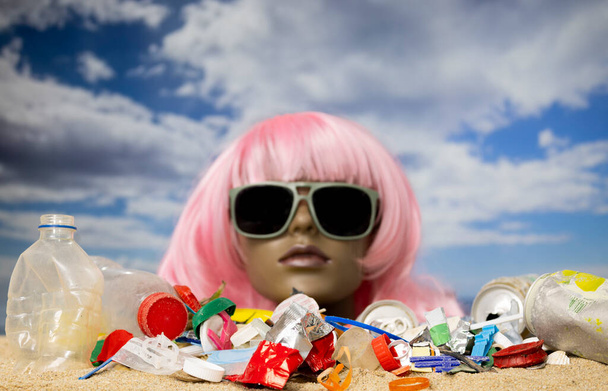 Plastová samičí figurína hlava uvízla v písku s pláží plnou odpadků a odpadků - Fotografie, Obrázek