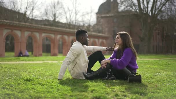 Διαφυλετικό ζευγάρι κρέμεται έξω κάθεται στο γρασίδι στο πάρκο - Πλάνα, βίντεο