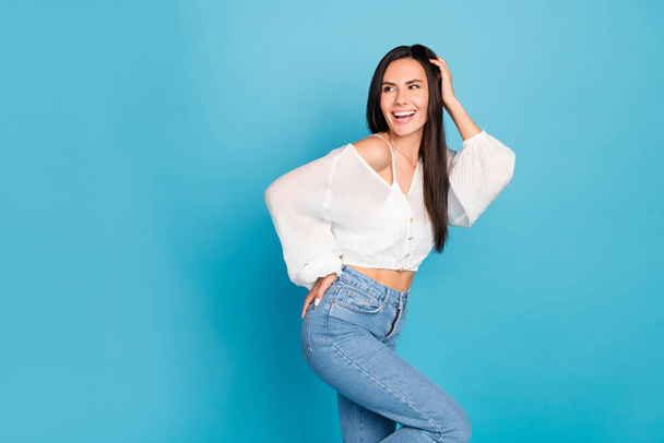 Photo of pretty excited girl dressed white blouse smiling adjusting hair looking back empty space isolated blue color background. - Foto, imagen