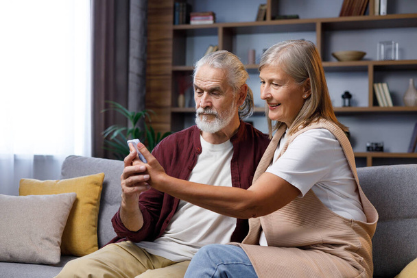 Mature happy couple communicates online call. A gray-haired husband and wife are talking to relatives on the phone. Video call on smartphone. Remote communication. - Φωτογραφία, εικόνα