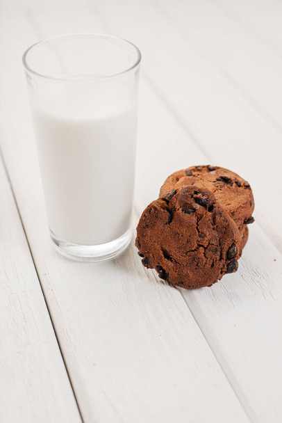 Egy pohár tejet csokis sütivel egy könnyű asztalon. - Fotó, kép