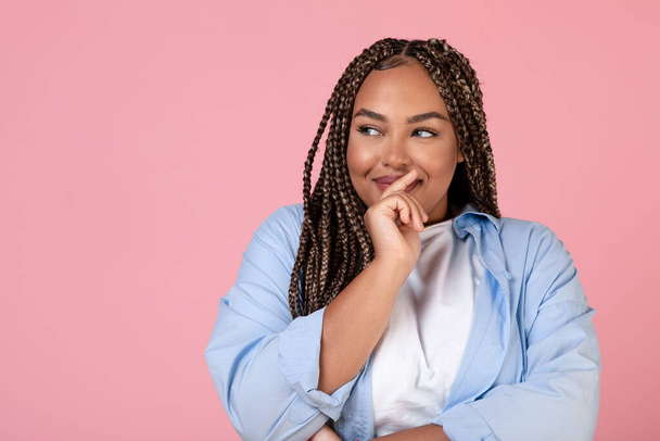 Retrato de feliz mulher negra obesa sonhando pensar em algo agradável olhando para além posando em pé no estúdio sobre fundo rosa. Conceito de Pensamentos Positivos - Foto, Imagem
