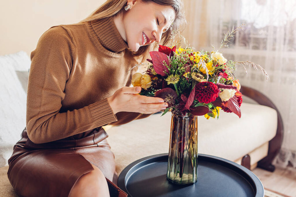Kobieta pachnie jesienny bukiet ze słoneczników Cynnia róż dalia kwiaty ułożone w wazonie w domu. Świeże kwiaty w czerwonym żółtym pomarańczowym kolorze jesieni. Wnętrze i wystrój salonu - Zdjęcie, obraz