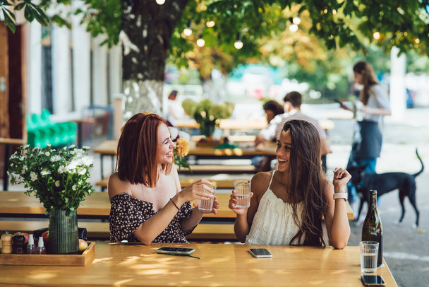 Twee mooie jonge vriendinnen praten in een café, roddelen, vertellen samen nieuws. Vrouwelijke vriendschap - Foto, afbeelding