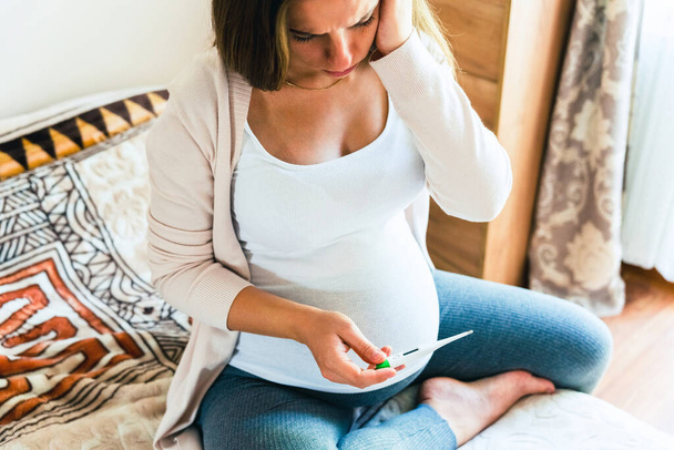 Проверка температуры термометра беременной. Беременная женщина держит термометр, проверяет температуру гриппа. Беременная больна. Концепция беременности, материнства, ожидания рождения ребенка - Фото, изображение