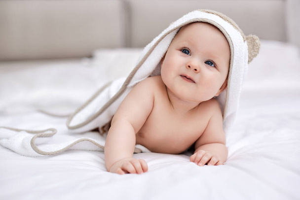 adorable baby girl lies on white bed with towel on her head and body after bath. Hygiene and baby care concept. - Fotoğraf, Görsel