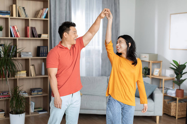 Amour romantique asiatique couple profiter du temps ensemble à la maison, danse valse, heureux chinois d'âge moyen homme et jolie jeune femme en vêtements de maison tenant la main et souriant à l'autre, copier l'espace - Photo, image