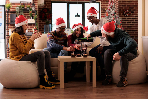 I coworkers versano occhiali di vino a evento di Natale, sentendosi festivi e felici a festa il giorno di vigilia di Natale in posto di lavoro con ornamenti di vacanza. Bere alcolici alla festa invernale. - Foto, immagini