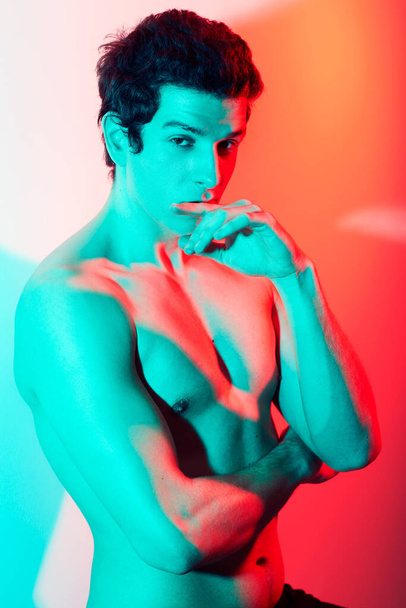 The face of confidence. A bare chested caucasian male looking at the camera covered by the tinge of a red and blue light - Фото, изображение