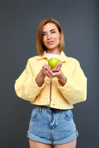 beautiful blonde woman holding green apple isolated on gray background. - Фото, изображение