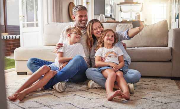 Relax, phone and selfie by happy family on living room floor, bonding and taking photo in their home together. Love, children and parents enjoying time together, having fun and smile for pictures. - 写真・画像