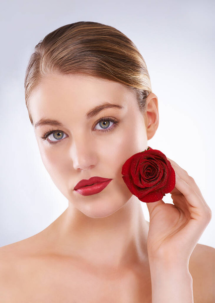 Roses are red and such a beauty is rare. Studio shot of a beautiful woman holding a rose next to her face - Фото, зображення