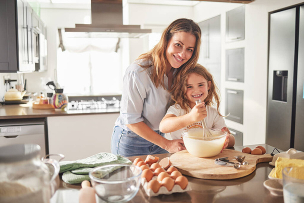 Mother with child in portrait and cooking breakfast in kitchen together for love, care and support with happiness. Smile of a young mom teaching, girl or kid learning to make food with eggs and flour. - Photo, Image