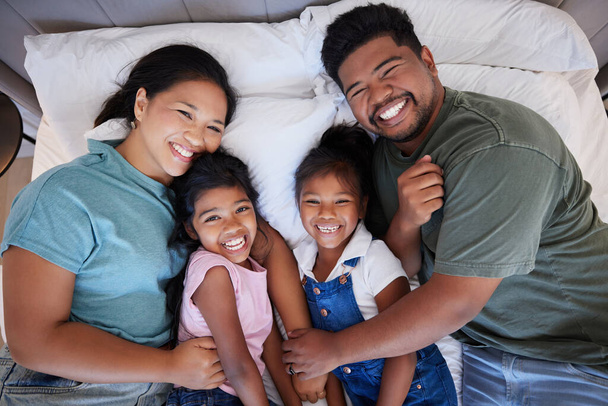 Una familia negra feliz en la cama, mamá y papá sostienen a los niños con amor. En su dormitorio en casa, los niños pequeños se ríen mientras los padres los abrazan con una sonrisa en sus rostros y disfrutan del tiempo de calidad en casa juntos. - Foto, imagen