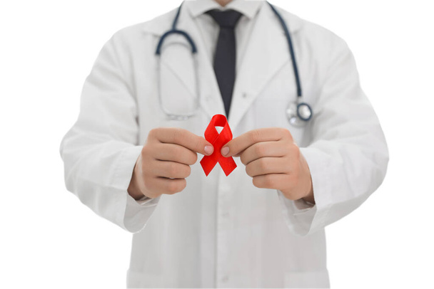 Doctor holding red ribbon on blurred background, closeup. AIDS awareness month - Fotó, kép