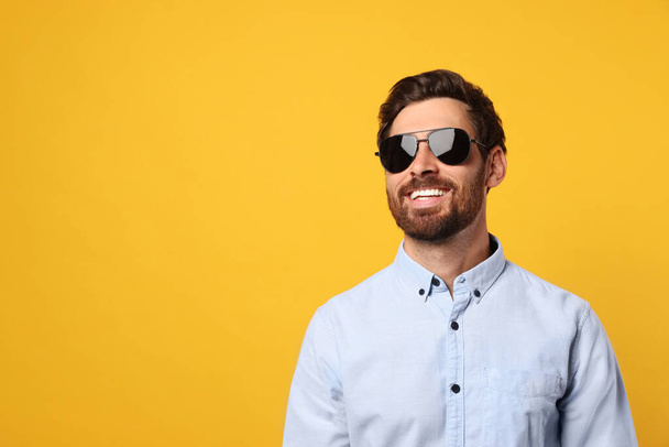Portrait of smiling bearded man with stylish sunglasses on orange background. Space for text - Foto, immagini
