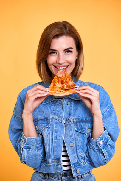mujer feliz mordiendo rebanada de pizza sobre fondo amarillo - Foto, Imagen
