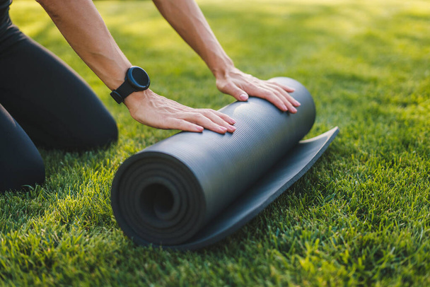 Cropped image of female hands folding exercise mat before working out in the park. Equipment for fitness. Healthy active lifestyle. Healthy activity. Training - Valokuva, kuva