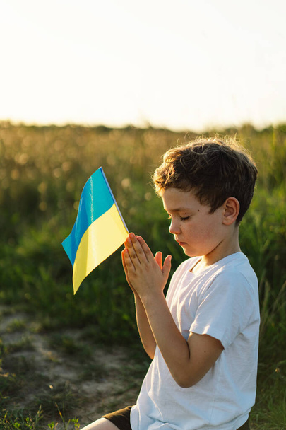 Украинский мальчик закрыл глаза и молился, чтобы остановить войну на Украине в поле на закате. Руки сложены в молитвенной концепции веры, духовности и религии. Война России против Украины. Остановить войну - Фото, изображение