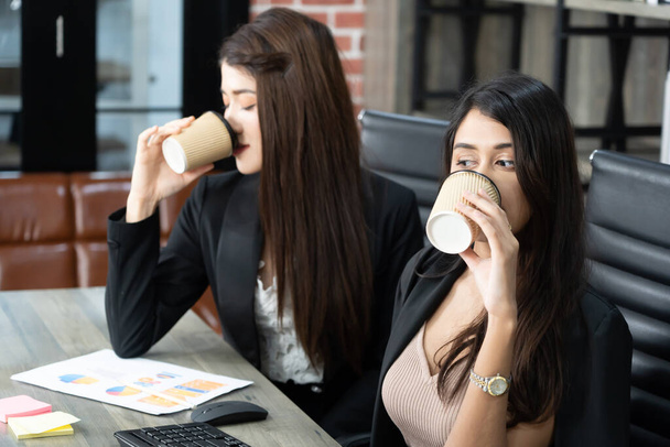 Pausa para café no escritório com duas colegas sentadas conversando sobre xícaras de café. Asiático mulher de negócios segurando xícara de café no escritório. - Foto, Imagem