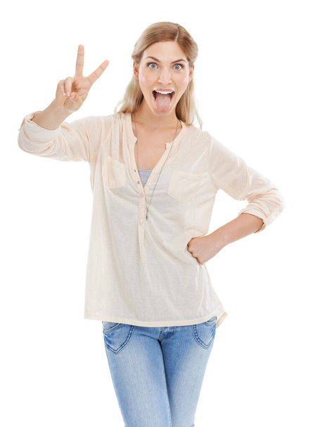 Maradj funky. Stúdió lövés egy vonzó fiatal nő mutatja a béke jele, miközben kinyújtja a nyelvét, hogy a fehér háttér - Fotó, kép