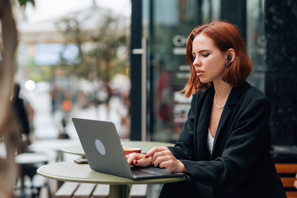 Mooie roodharige vrouw werken op laptop in openlucht cafe - Foto, afbeelding