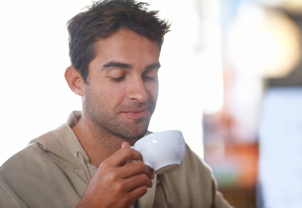 Ez egy jó sült. Egy fiatalember érzi a kávéját, miközben egy kávézóban ül. - Fotó, kép