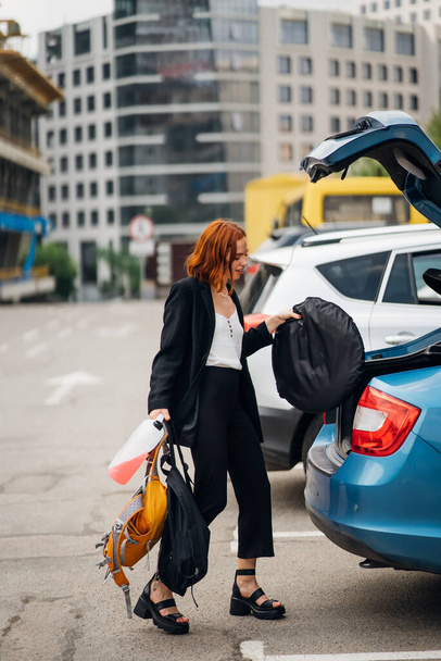 A young woman is packing luggage into the car trunk - Fotó, kép