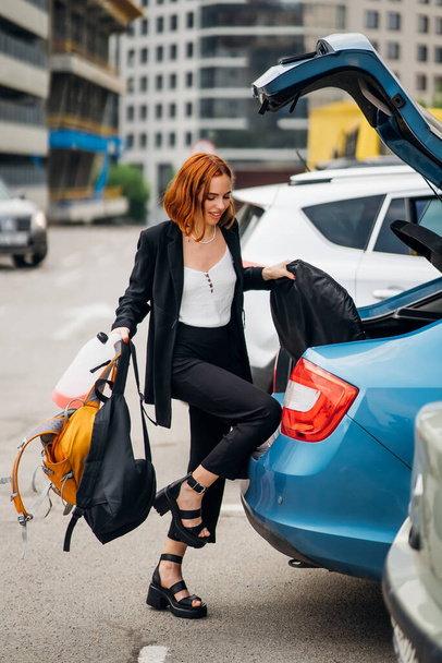 A young woman is packing luggage into the car trunk - 写真・画像