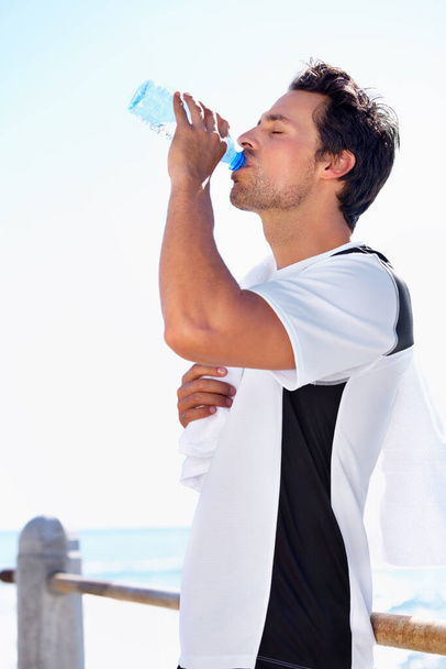 Mantener hidratado. Un joven en forma tomando un descanso acuático mientras hace ejercicio al aire libre - Foto, imagen