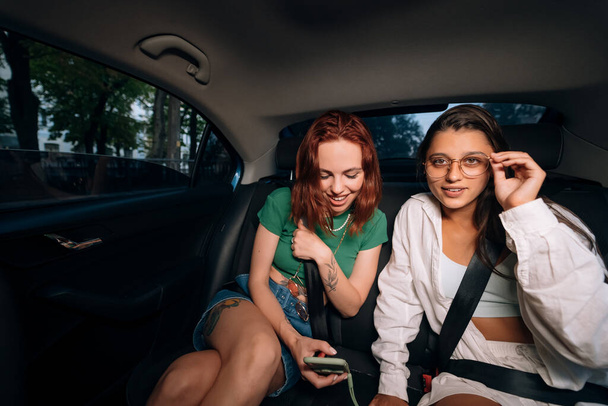 Vida real de amigos juntos en el asiento trasero de un taxi sosteniendo teléfonos celulares y revisando mensajes. - Foto, Imagen